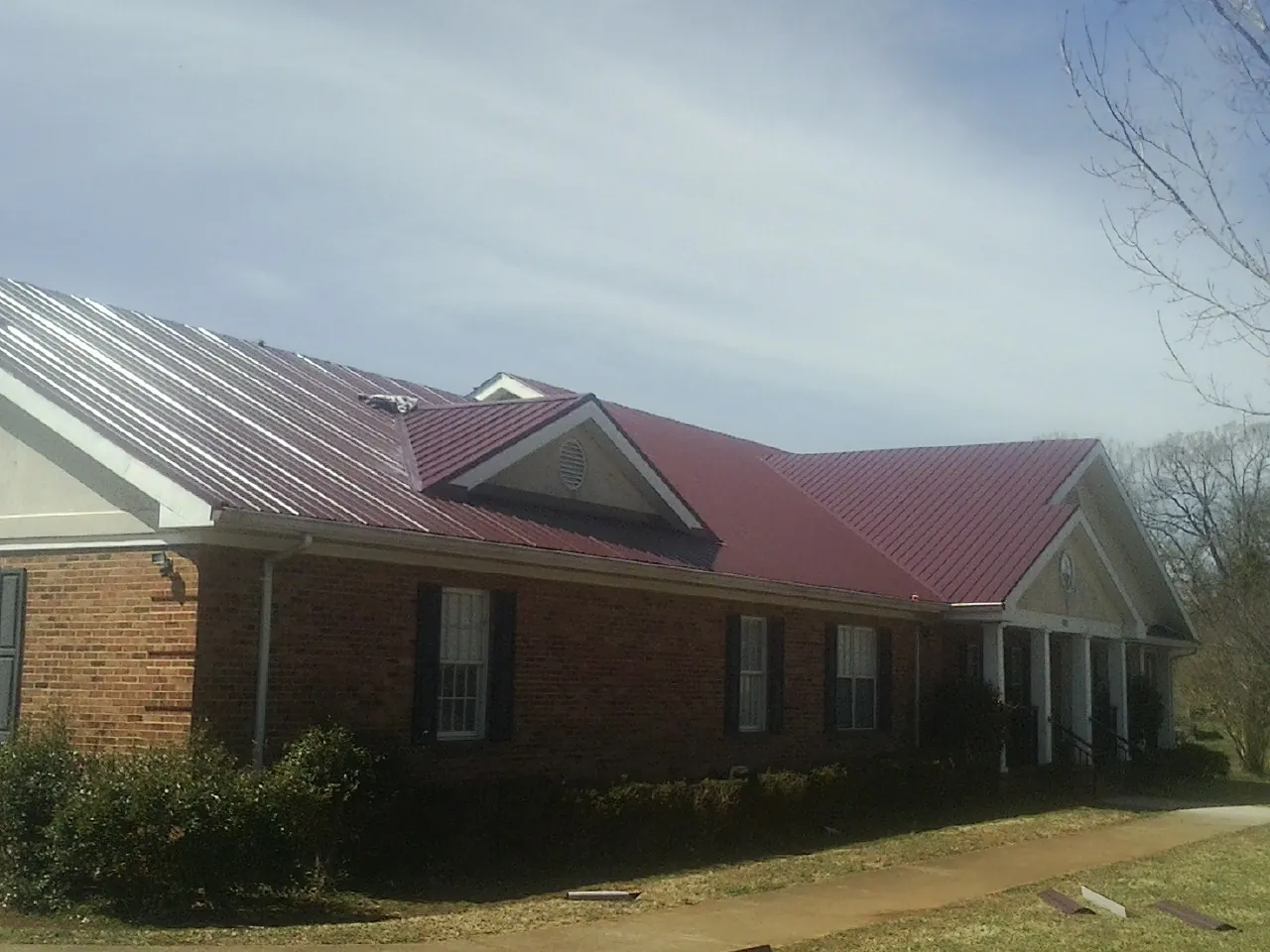 Red metal roof with gabled entries on a long brick building, from a Hail Damage Roof Repair job in Bay City