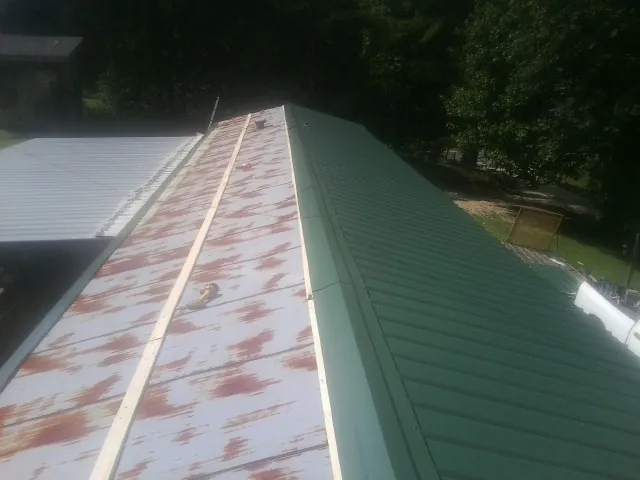 Old rusted panels beside newly installed green metal roofing — Wind Damage Roof Repair by Roofing Brothers in Bay City
