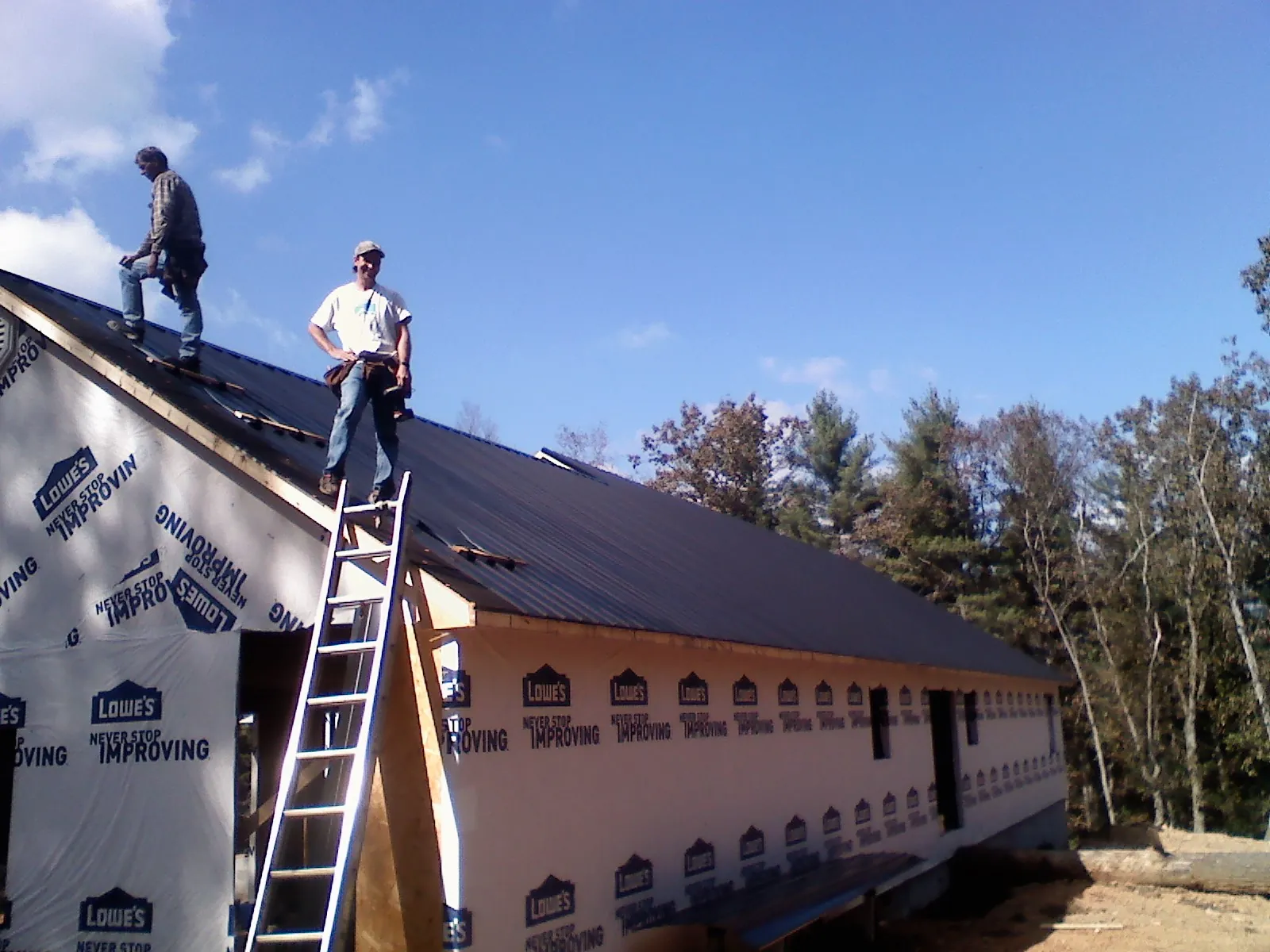 Two roofers standing on a long dark metal roof over a wrapped building in Bay City