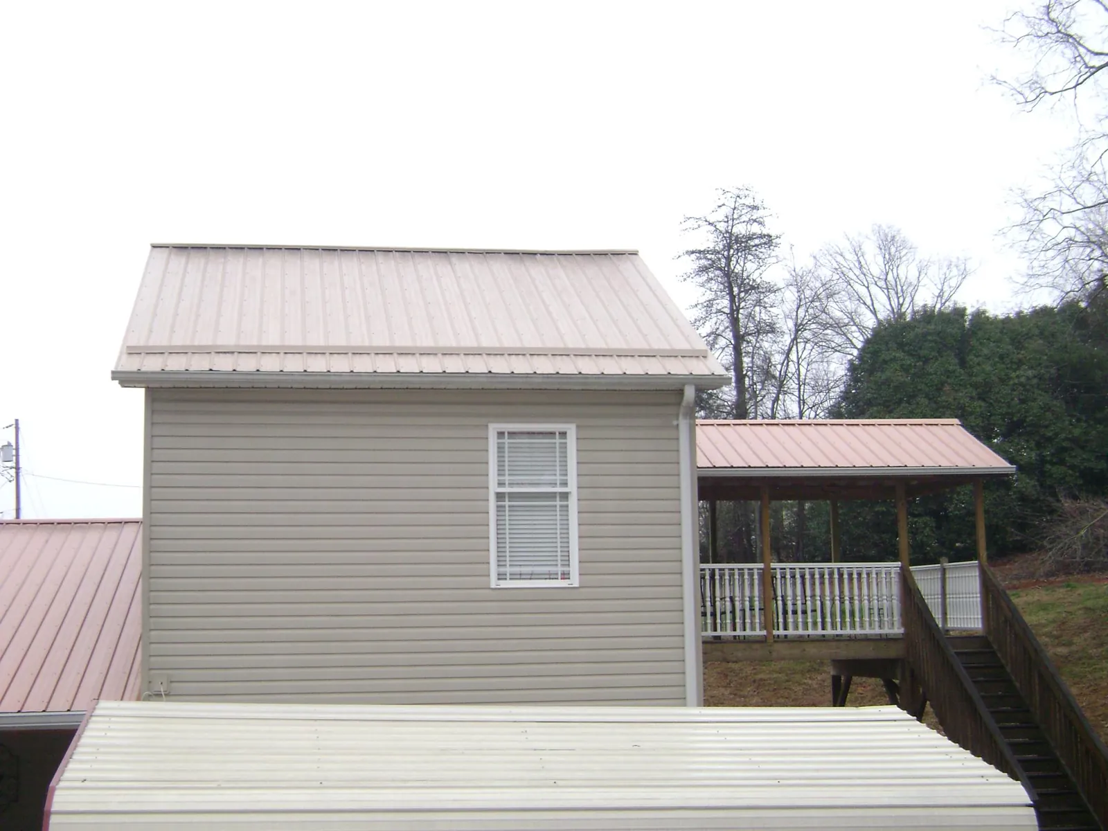 Tan metal roofs on a two story addition and attached porch, from a Roof Replacement job in Bay City
